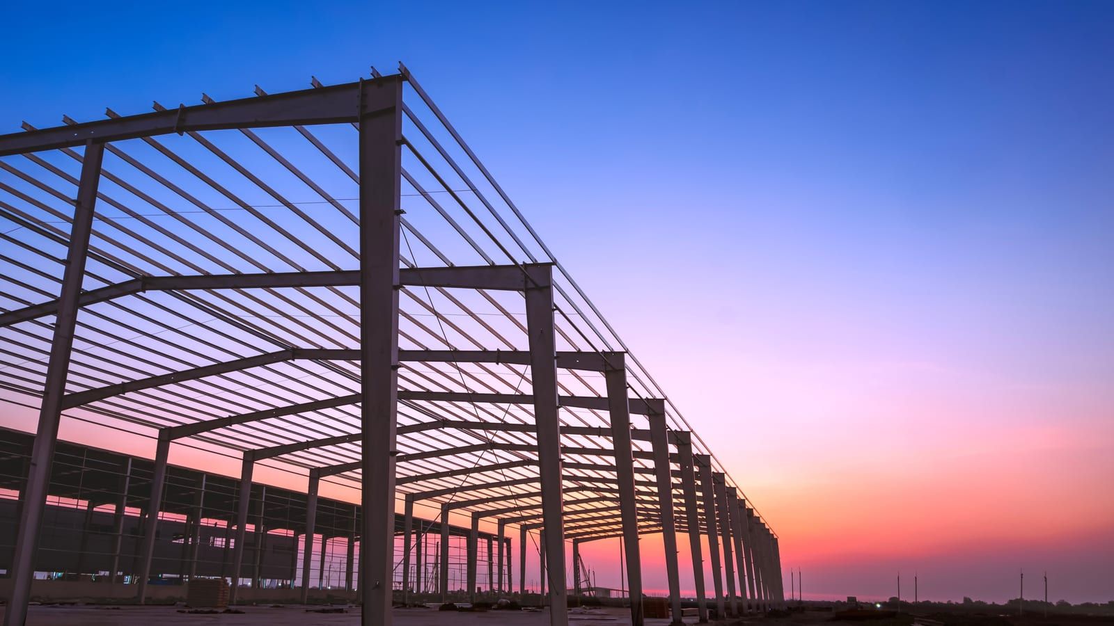 Estructura metálica de nave industrial en construcción al atardecer